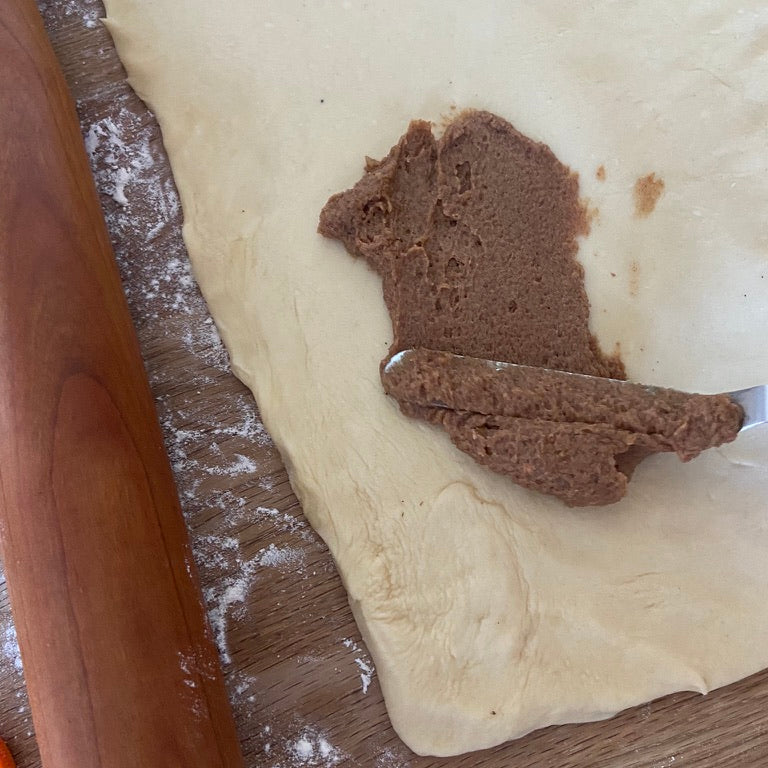 Dough with cinnamon filling being spread on it next to a rolling pin